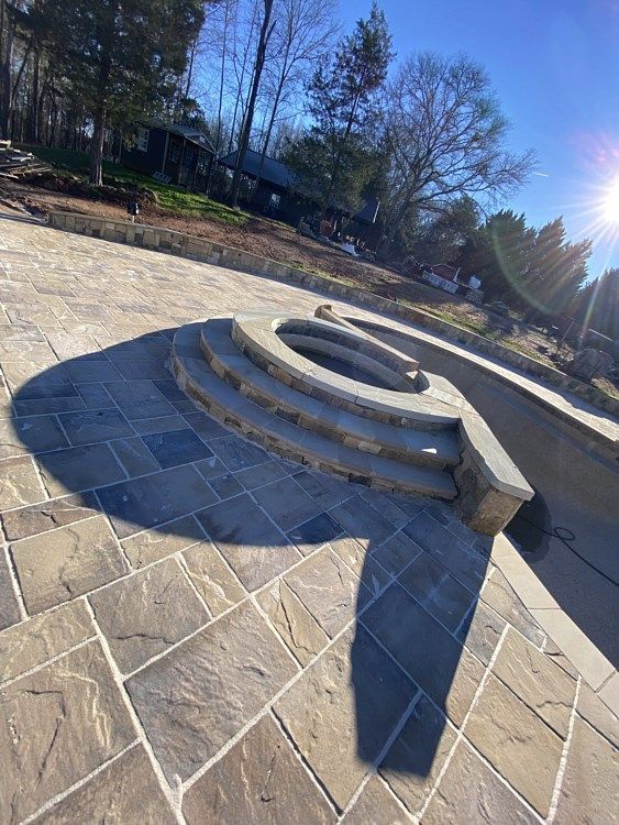 A stone patio with stairs and a fire pit in the middle of it.