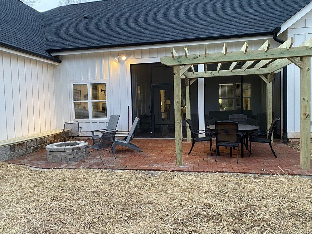 A patio with a pergola , table and chairs and a fire pit.