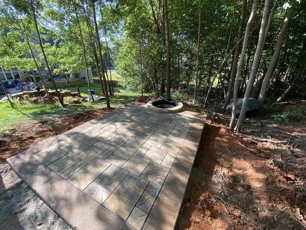 A patio with a fire pit in the middle of the woods.