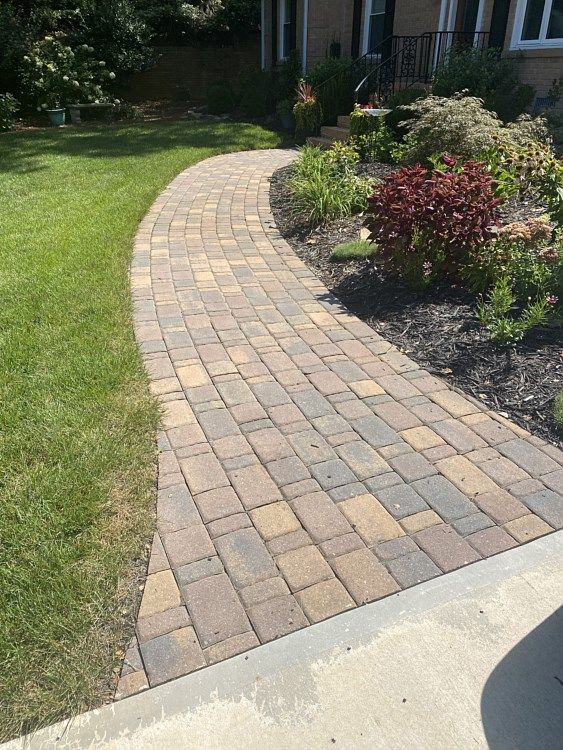 A brick walkway leading to a house with a lush green lawn.