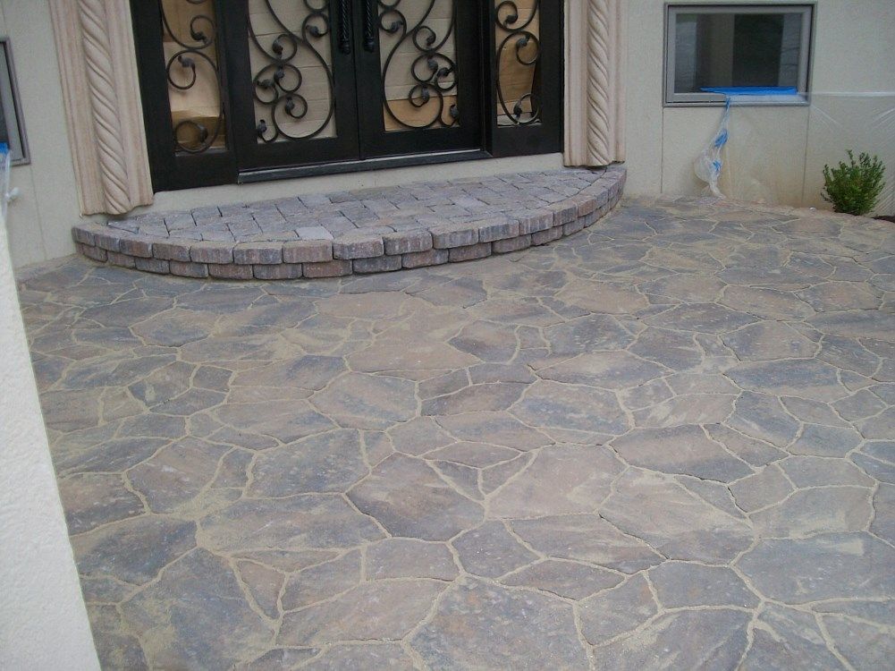 A stone patio in front of a house with a wrought iron door
