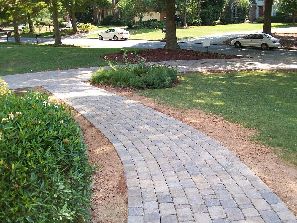 A white car is parked on the side of the road next to a brick walkway