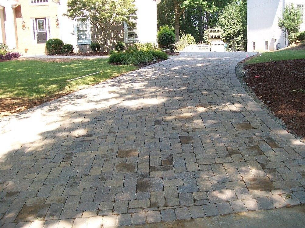 A brick driveway leading to a white house