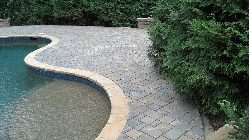 A swimming pool with a brick walkway surrounding it.