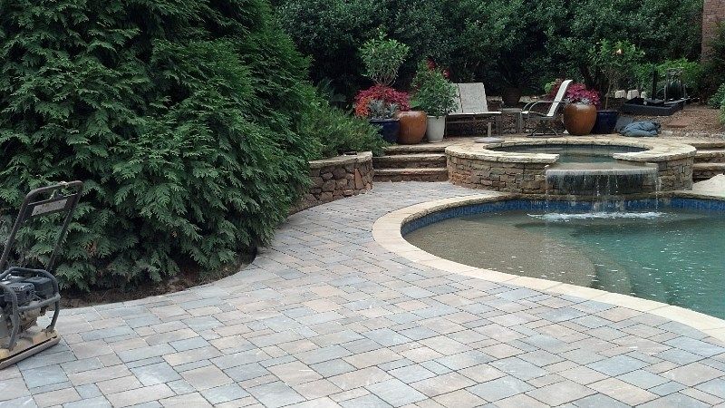A patio with a swimming pool and a waterfall in the backyard.