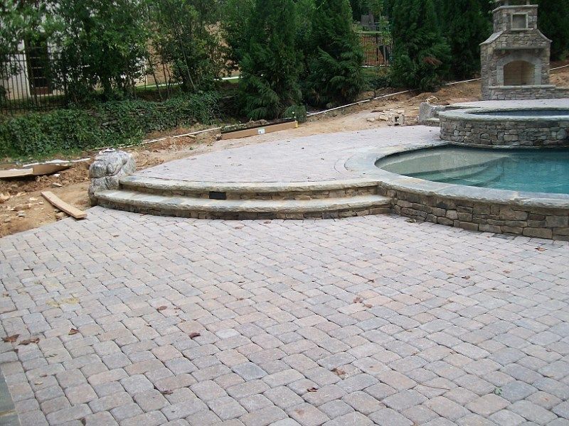A patio with steps leading to a pool and a fireplace