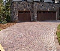 A brick driveway leading to a house with two garage doors.
