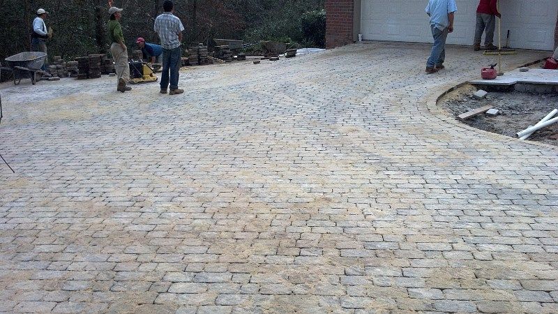 A group of people are standing on a brick driveway.