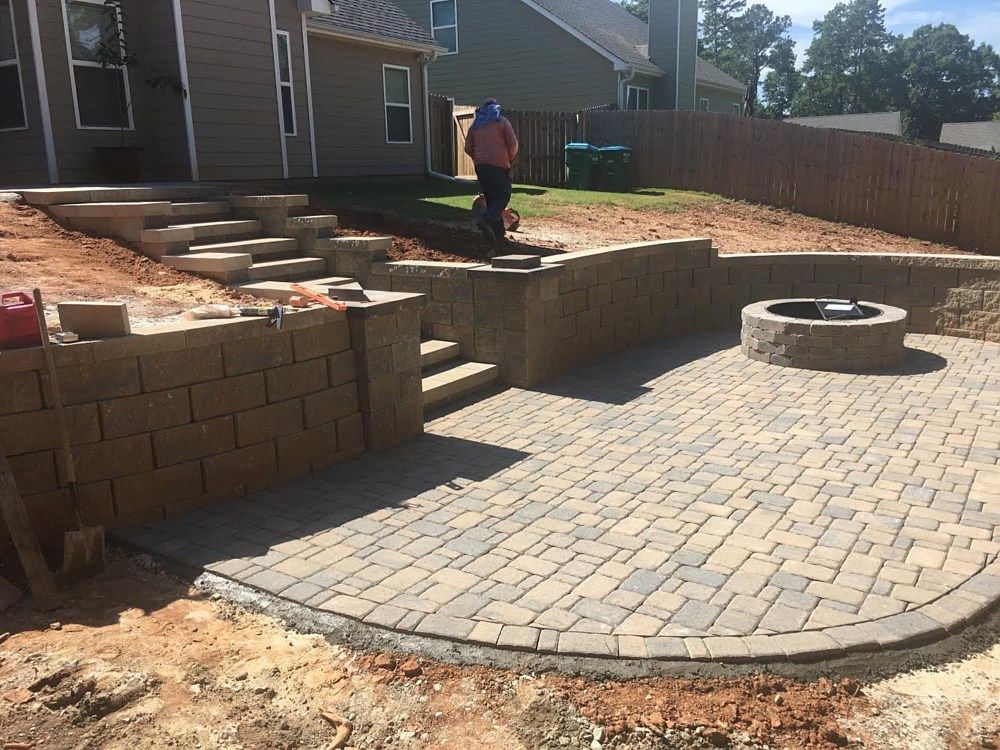 A man is standing on a brick patio next to a fire pit.