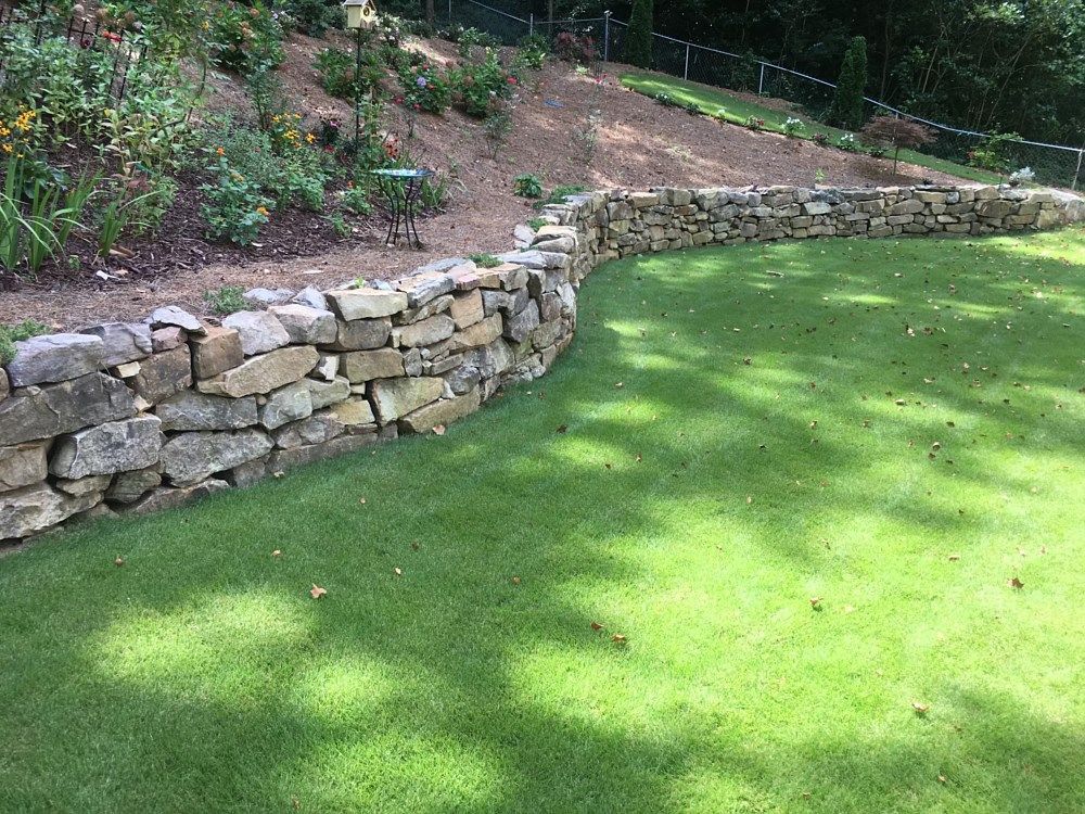 A stone wall surrounds a lush green lawn in a backyard.