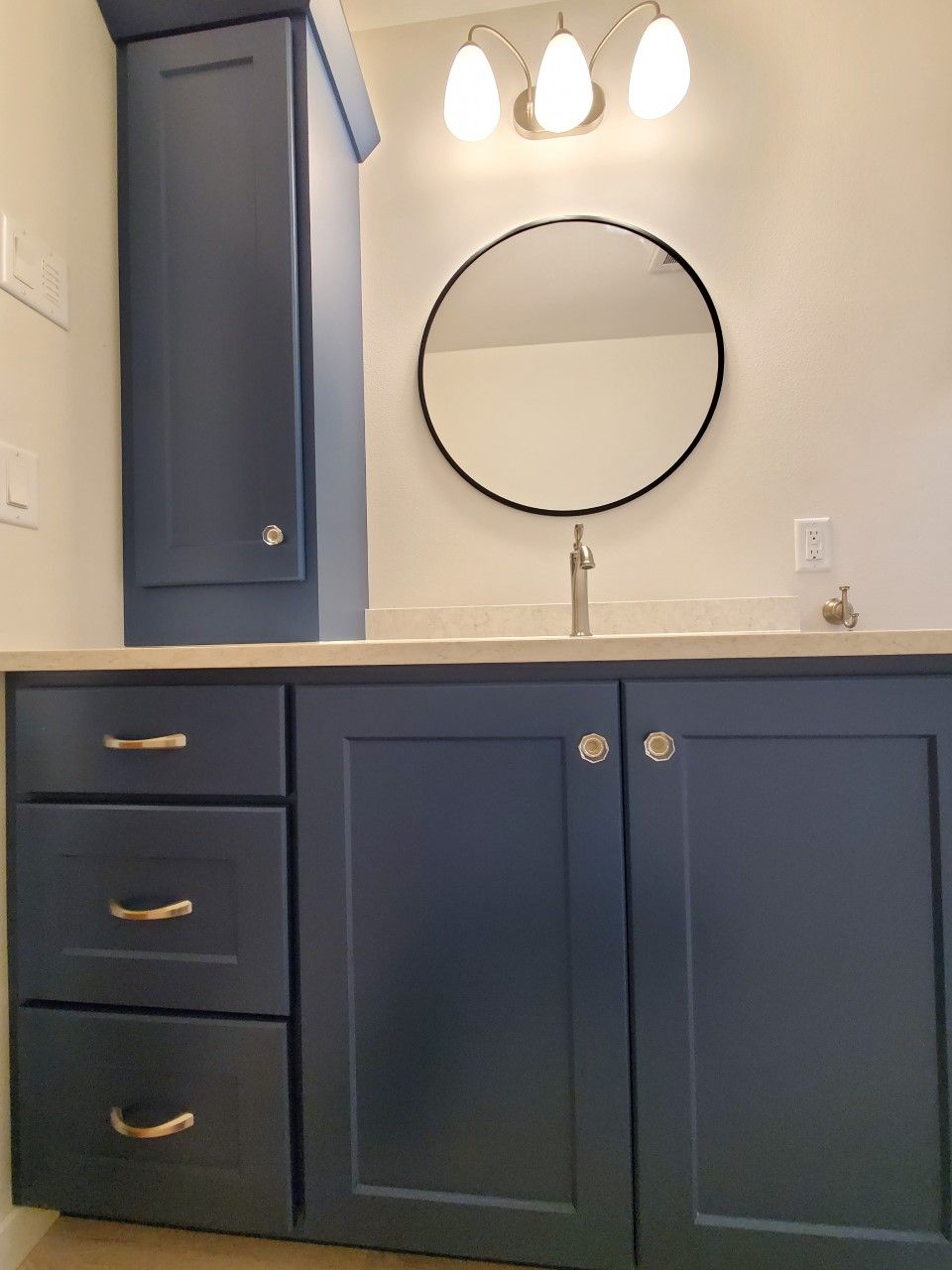 A bathroom with blue cabinets and a round mirror