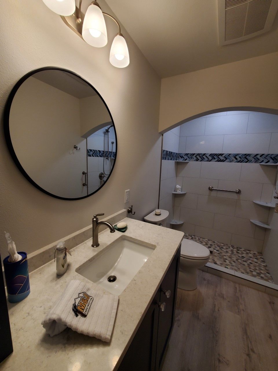 A bathroom with a sink a toilet and a round mirror