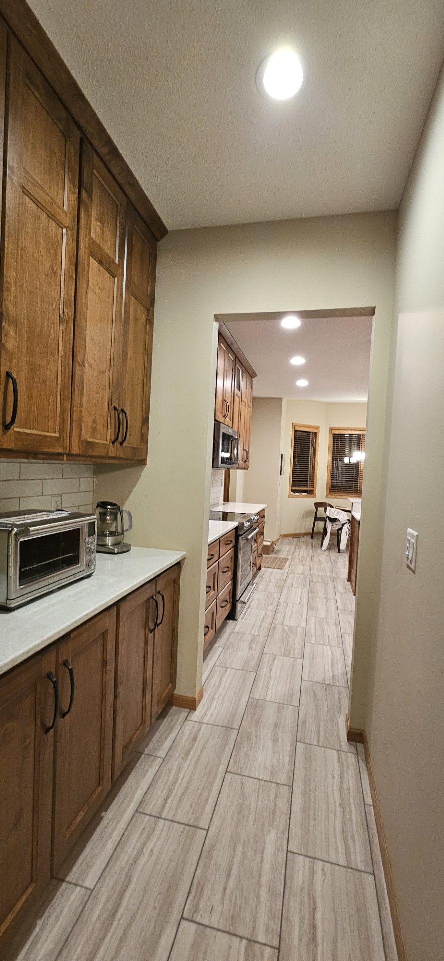 A long hallway leading to a kitchen with wooden cabinets and tile floors