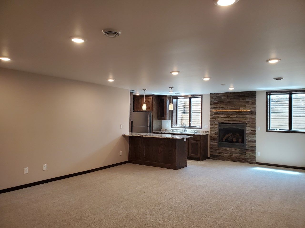 An empty living room with a fireplace and a kitchen