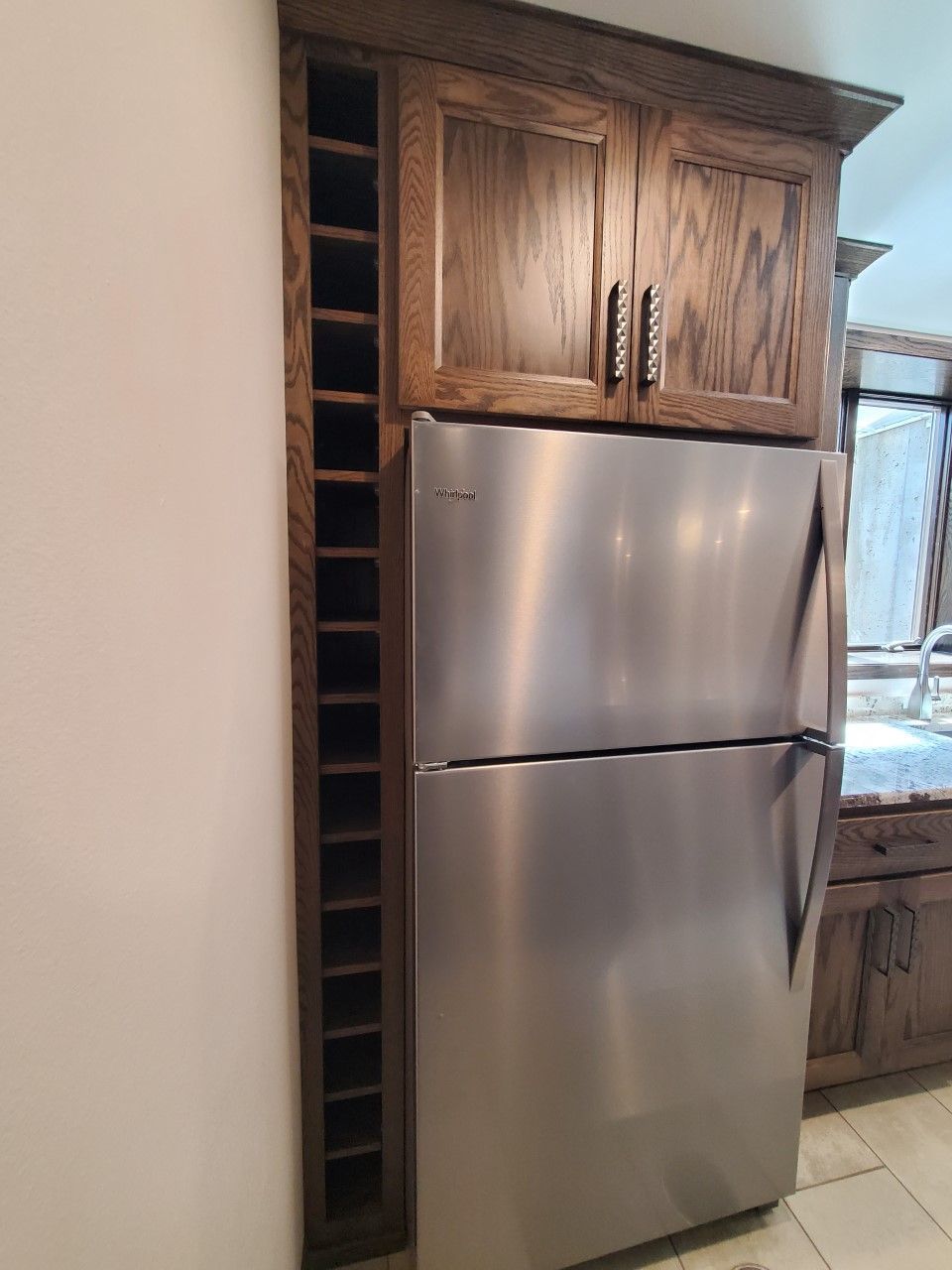 A stainless steel refrigerator is sitting in a kitchen next to a wine rack