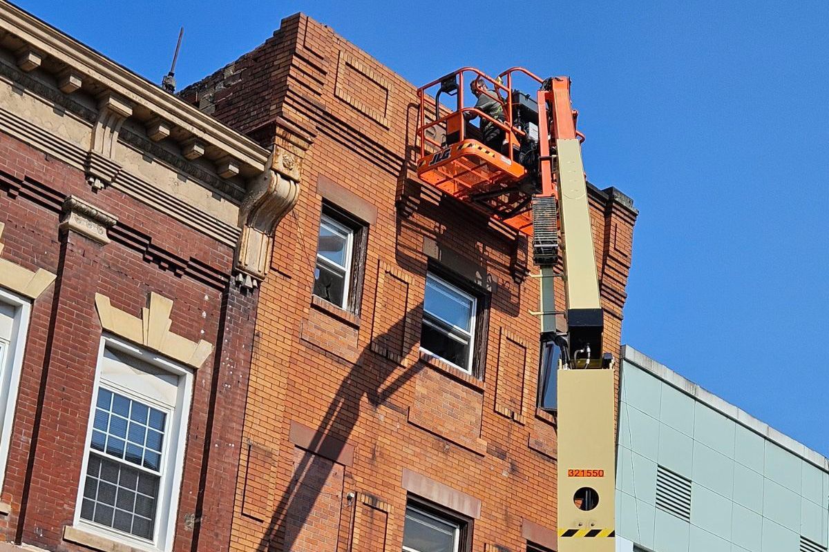 Person in an orange lift working on the brick exterior of a building with a blue sky in the background.