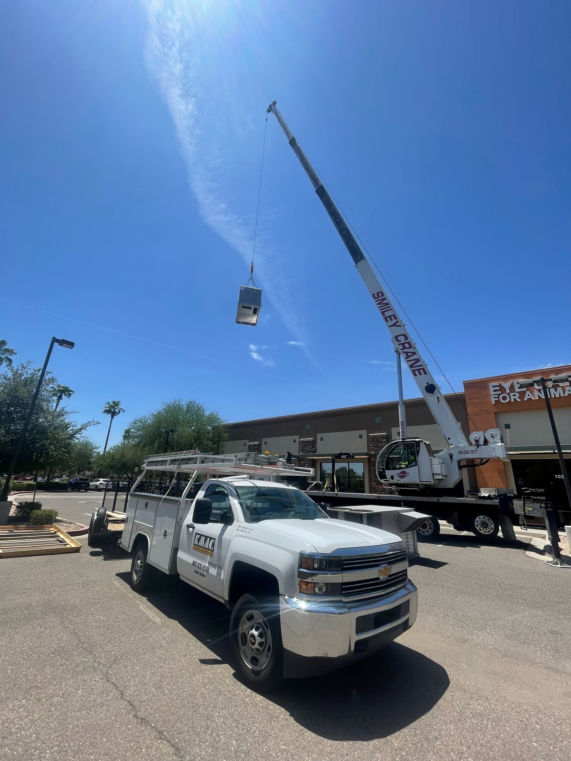 White crane lifting an object near a Home Depot and work truck on a sunny day.