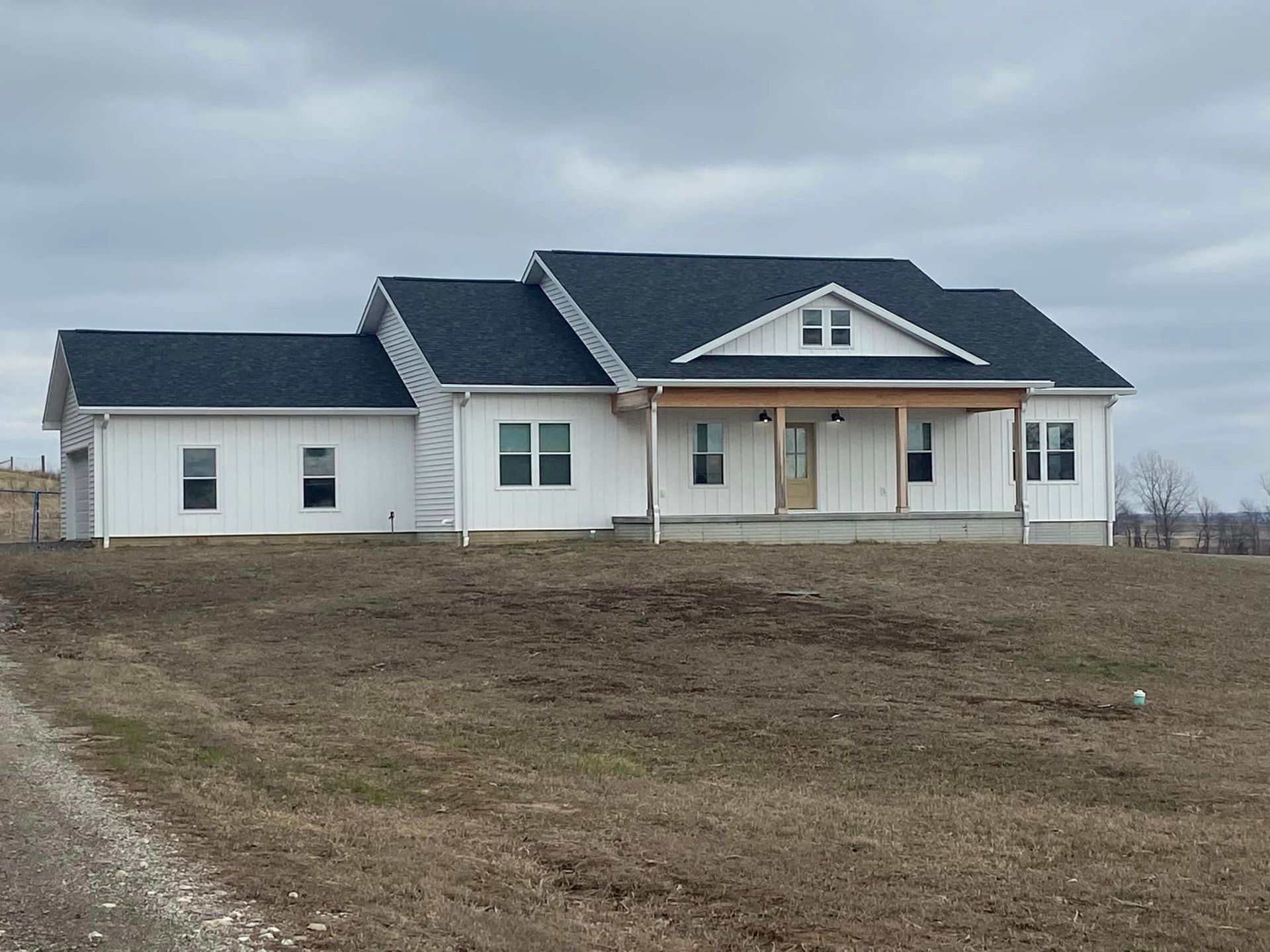 A white house with a black roof is sitting in the middle of a field.