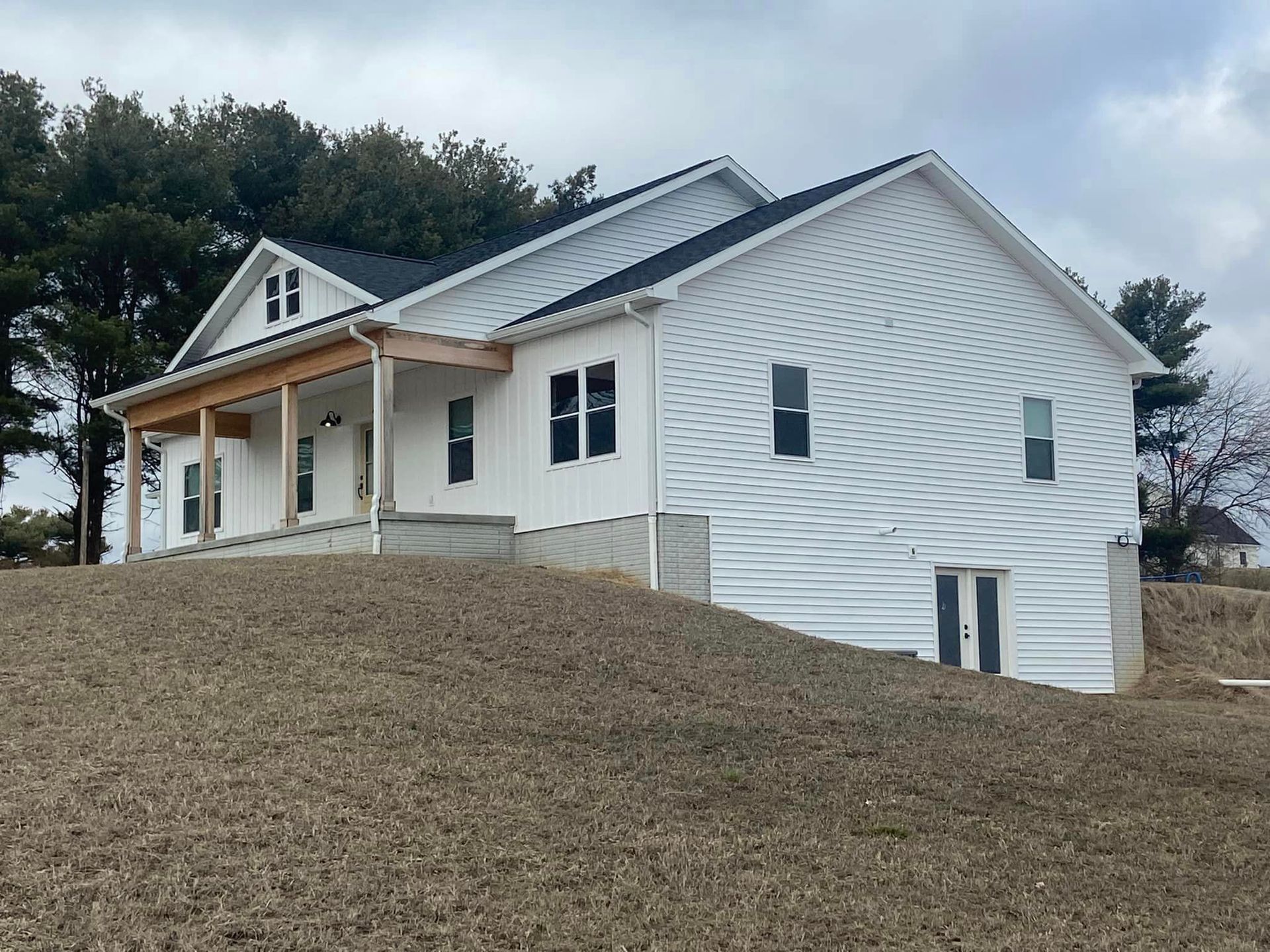 A white house with a porch is sitting on top of a dirt hill.