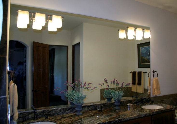 Bathroom with large mirror reflecting lights, two sinks, and a partially open doorway.
