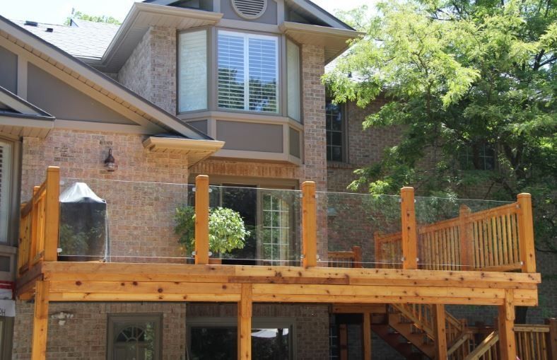 Wooden deck attached to a two-story brick house with glass railing and a sliding door.