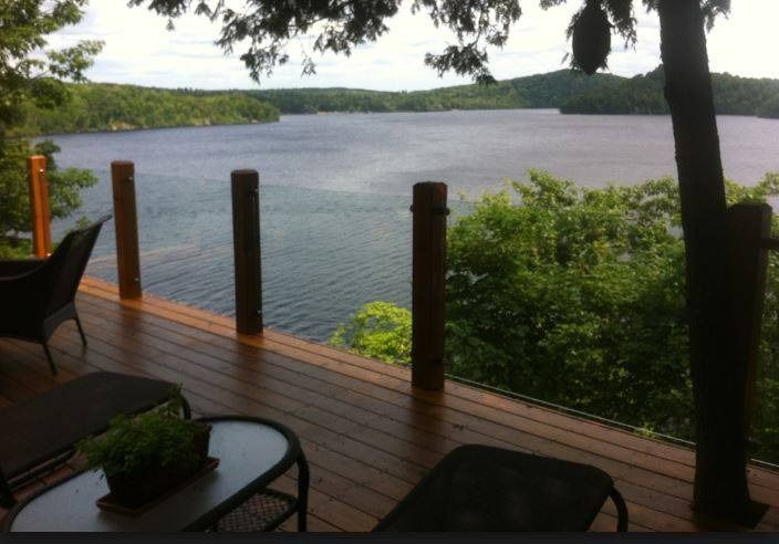 Wooden deck overlooking a lake with trees and rolling hills. Several chairs and a table are on the deck.