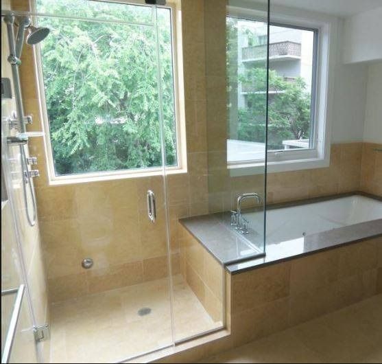 Bathroom with a walk-in shower and a bathtub next to a window; beige tiles, glass enclosure.