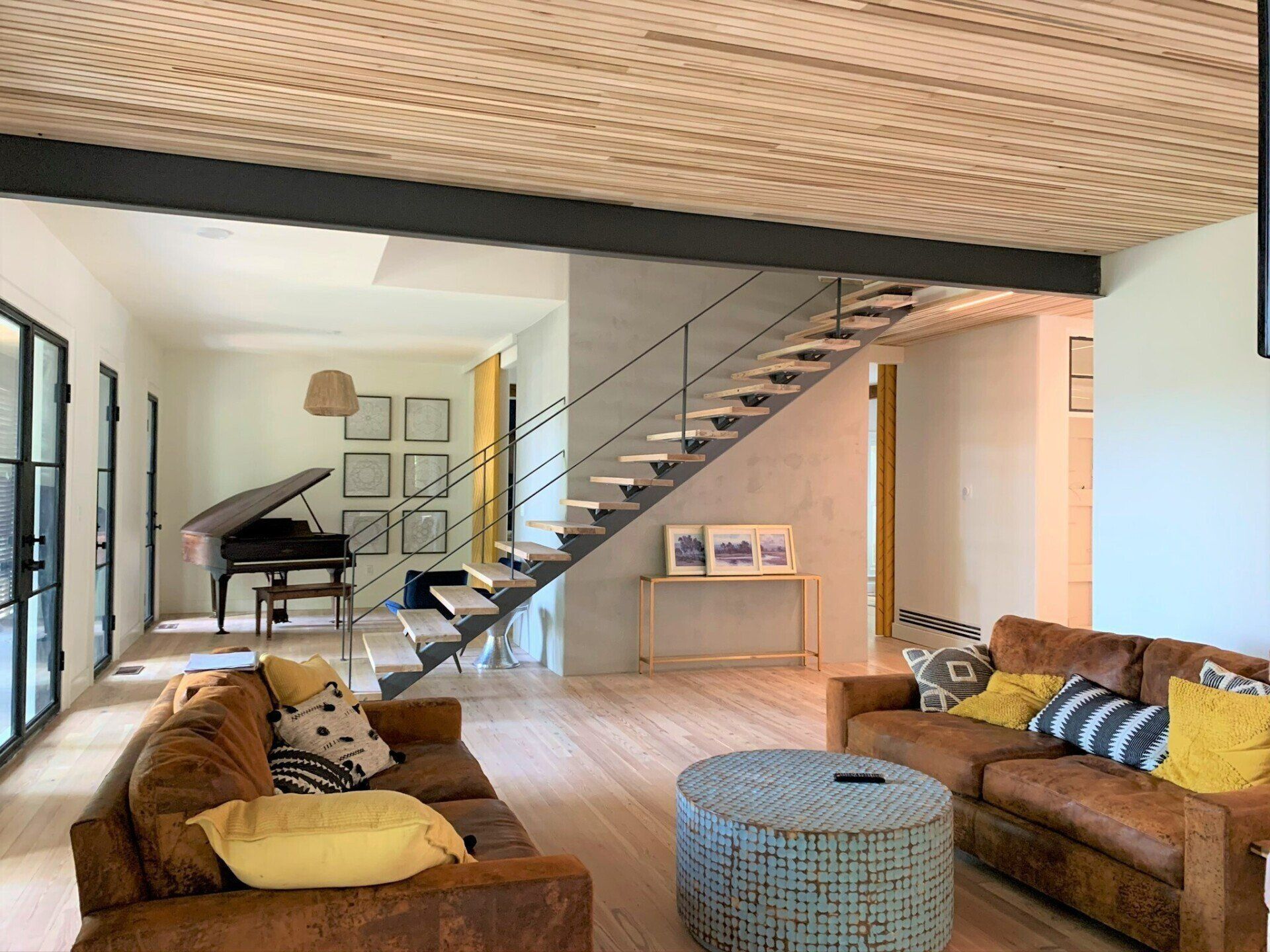A wooden floor living room with two couches, a piano, and a staircase.