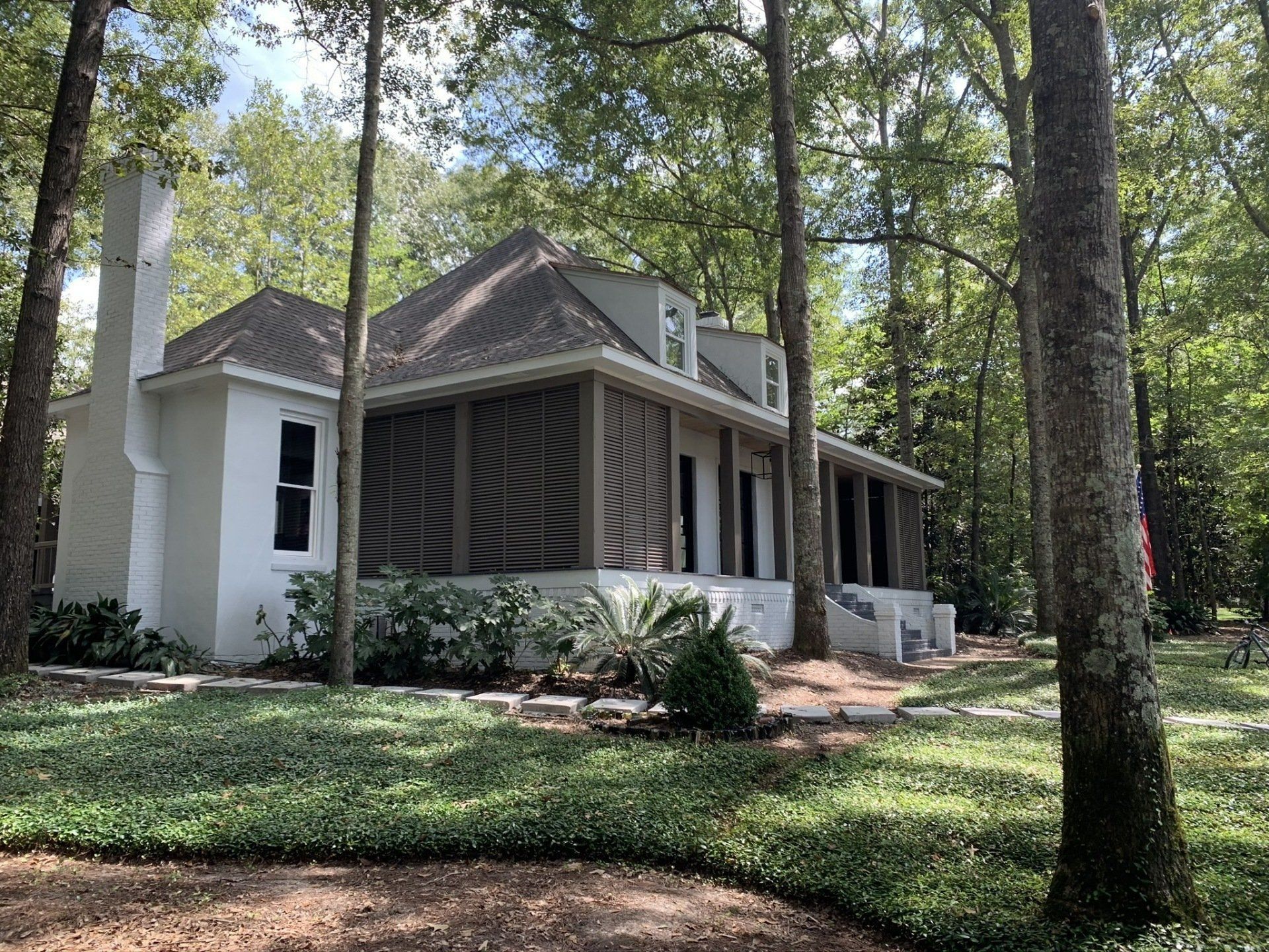 A white house with a porch is surrounded by trees.