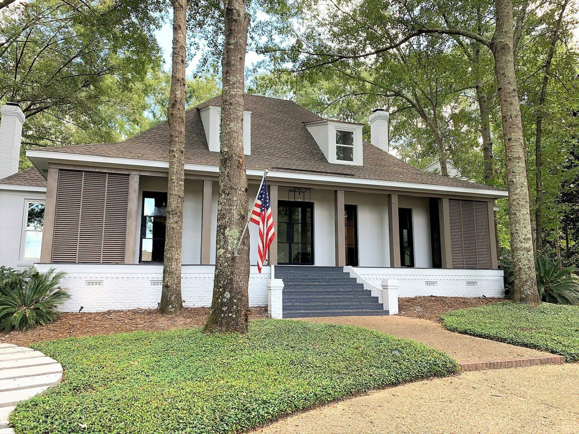 A white house with an american flag on the front porch surrounded by trees.