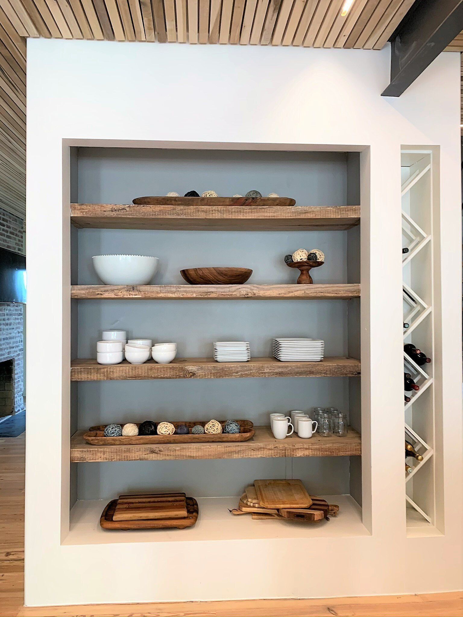 A wooden shelf filled with bowls, plates, and a wine rack.