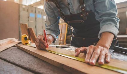 A man is measuring a piece of wood with a tape measure and a pencil.