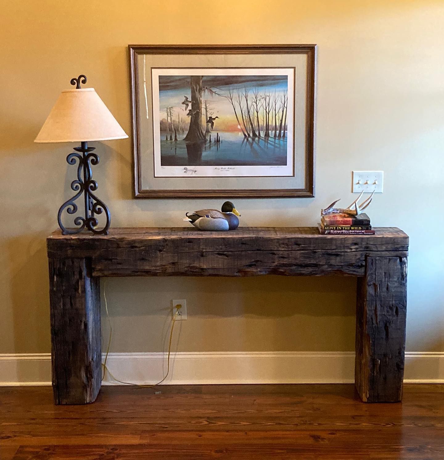 A wooden table with a lamp and a picture on the wall above it.