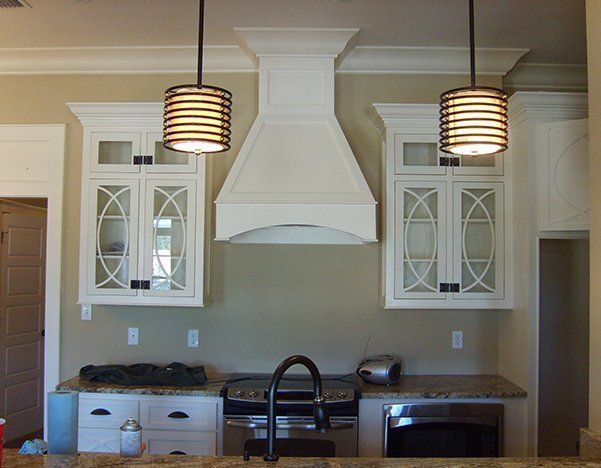 a kitchen with white cabinets, a stove, a sink, and a hood