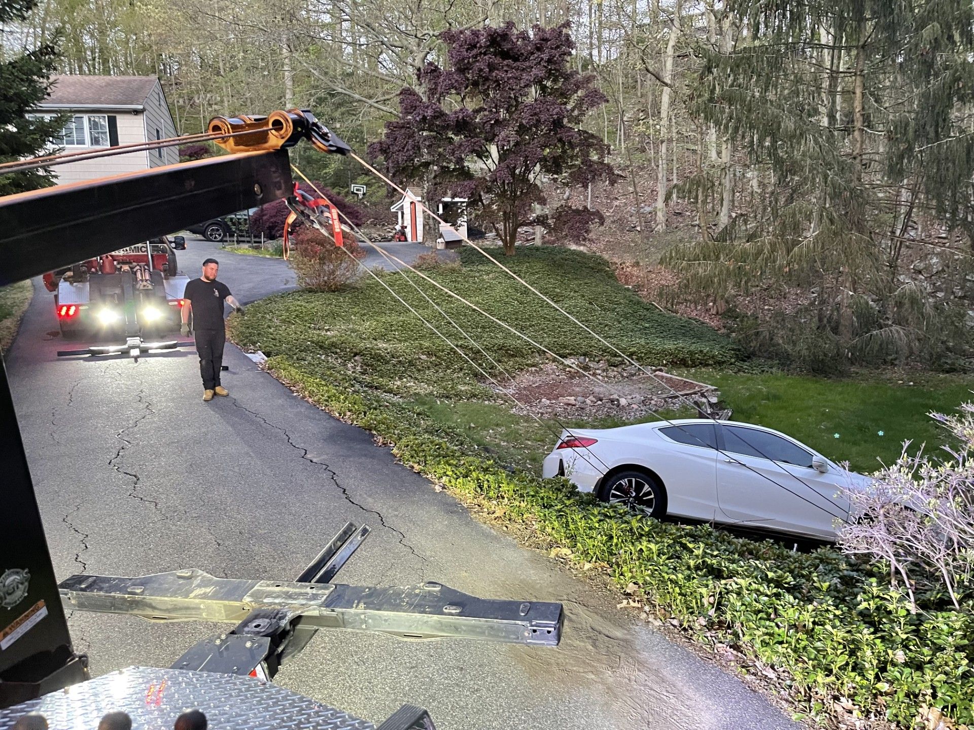 A white car is being towed down a road by a tow truck.