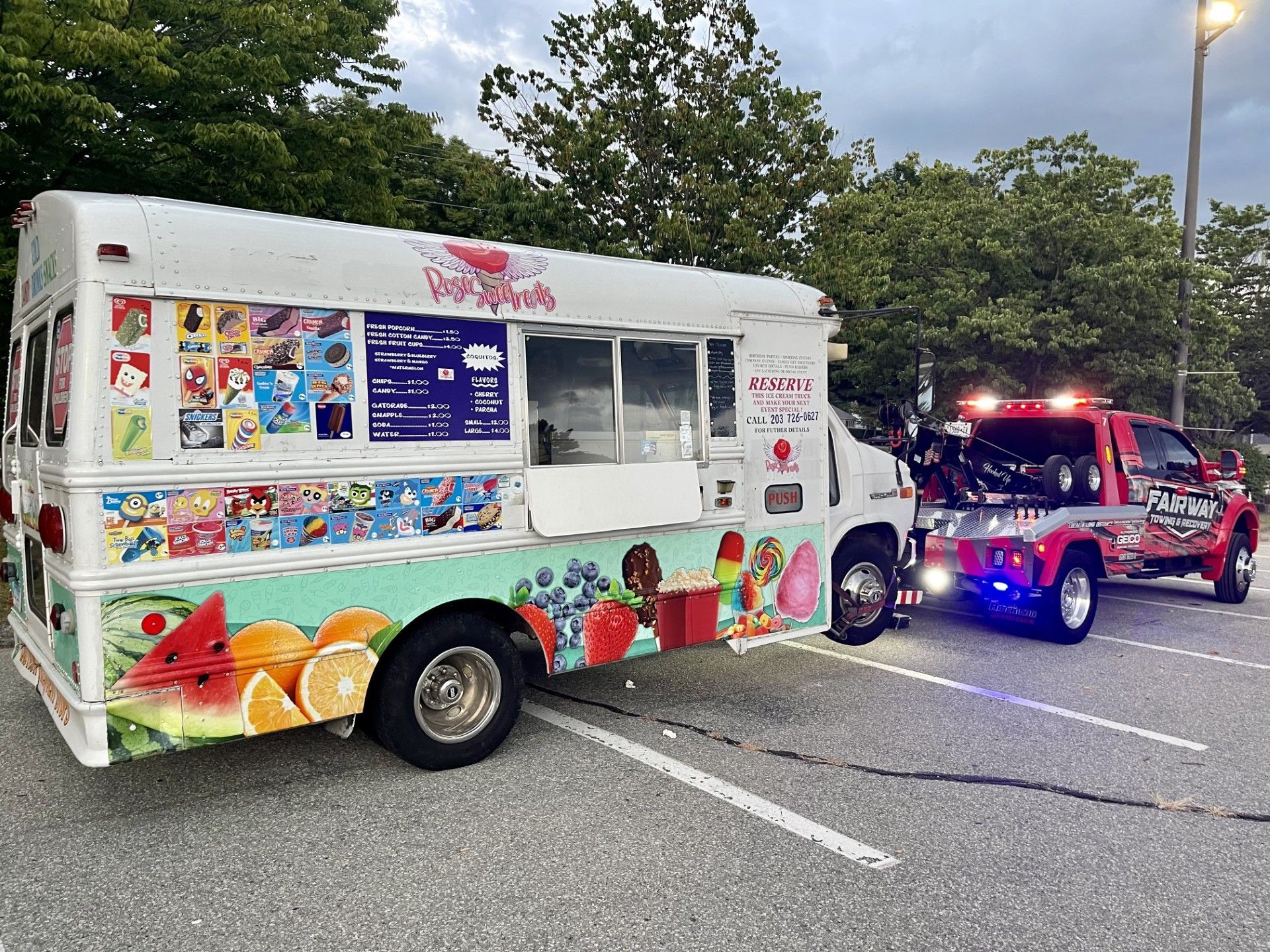 An ice cream truck is parked next to a tow truck in a parking lot.