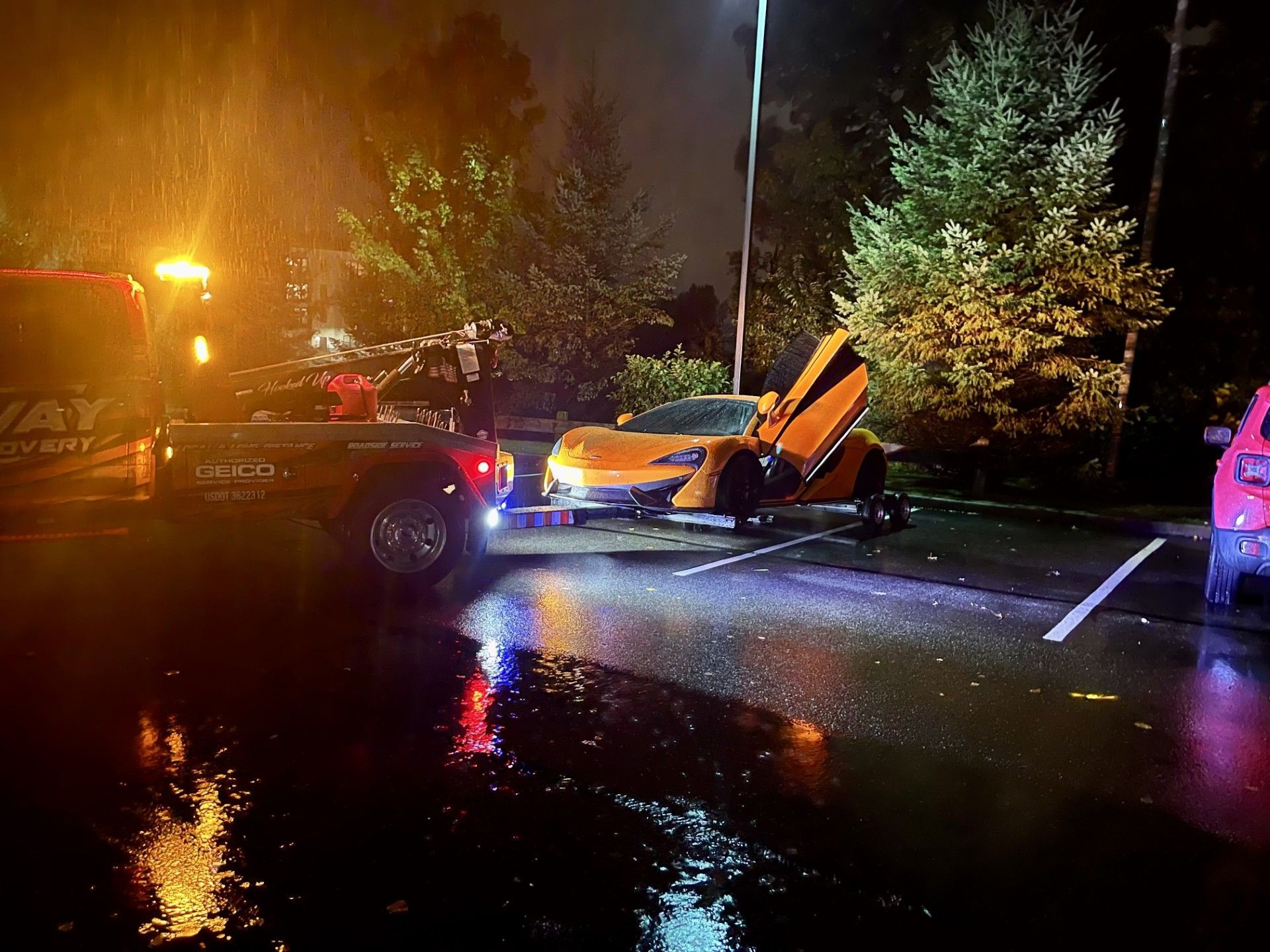 A car is being towed by a tow truck in a parking lot at night.