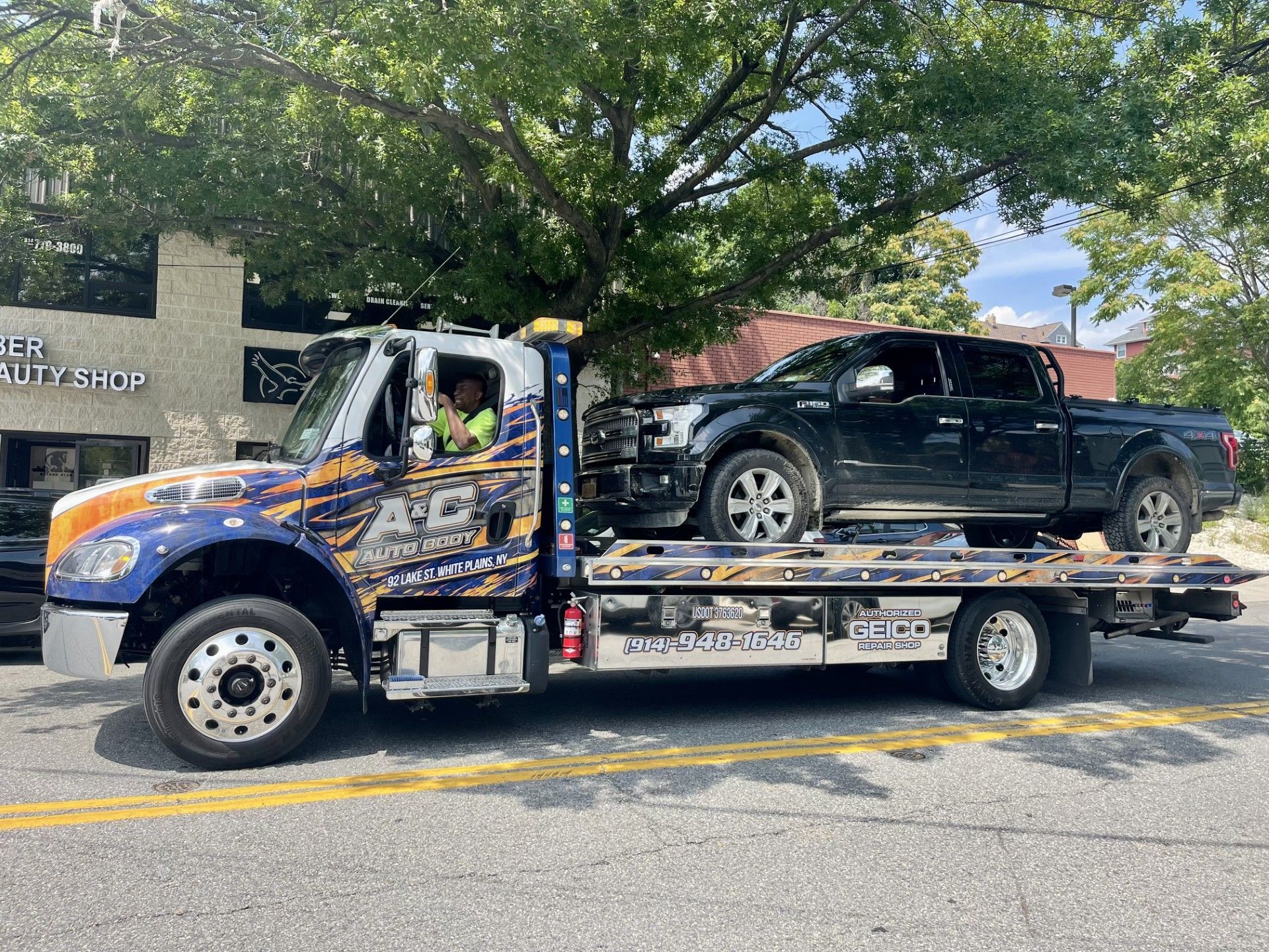 A tow truck with two trucks on the back is parked on the side of the road.