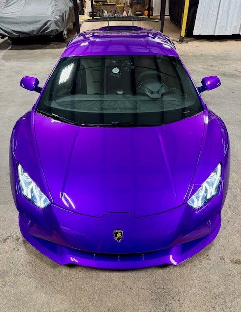 Purple Lamborghini sports car, front view, headlights on, in a garage.