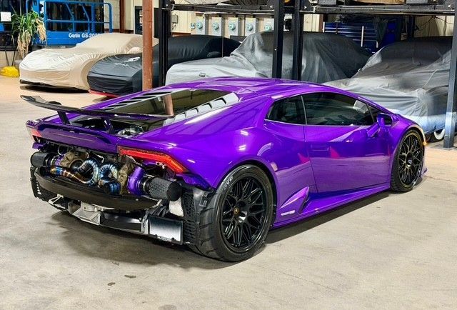 Purple Lamborghini Huracan, rear view, modified engine bay visible. Black wheels, indoor setting.