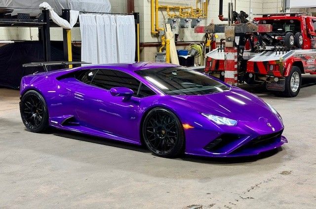 Purple Lamborghini sports car parked in a garage with a tow truck in the background.