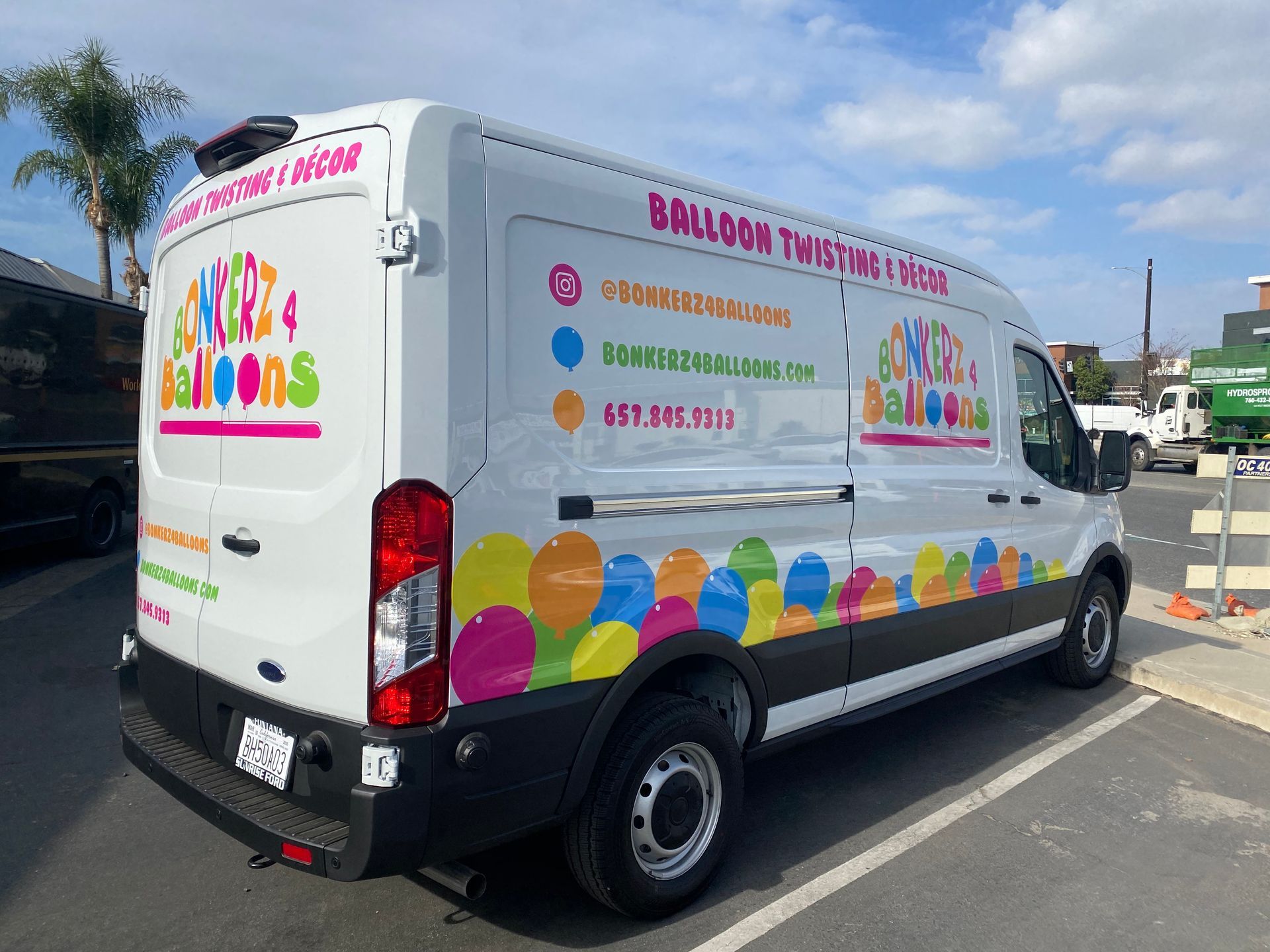 A white van with colorful balloons on the side is parked in a parking lot.