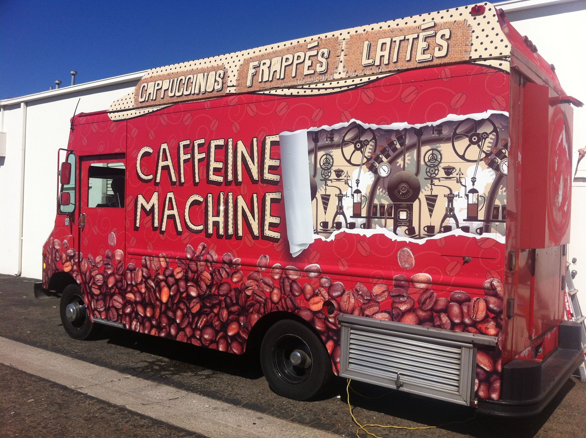 A red caffeine machine truck is parked in front of a building