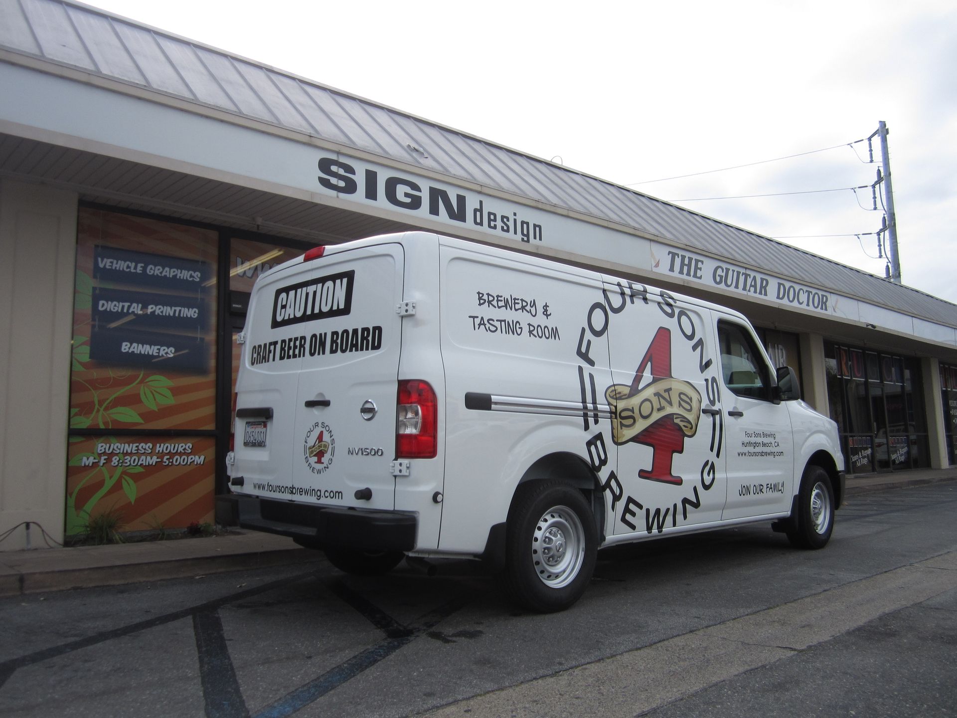 A white van is parked in front of a building that says sign design