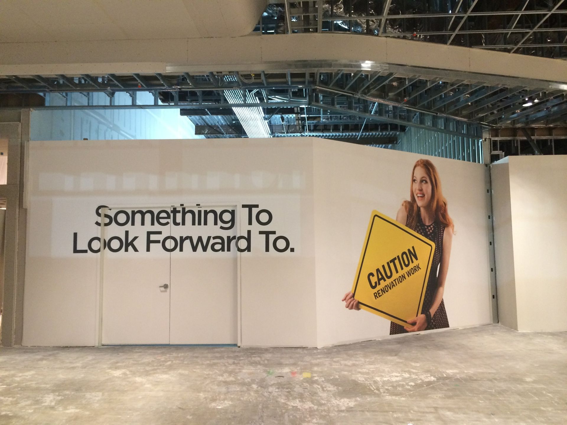 A woman is holding a caution sign in front of a wall that says something to look forward to