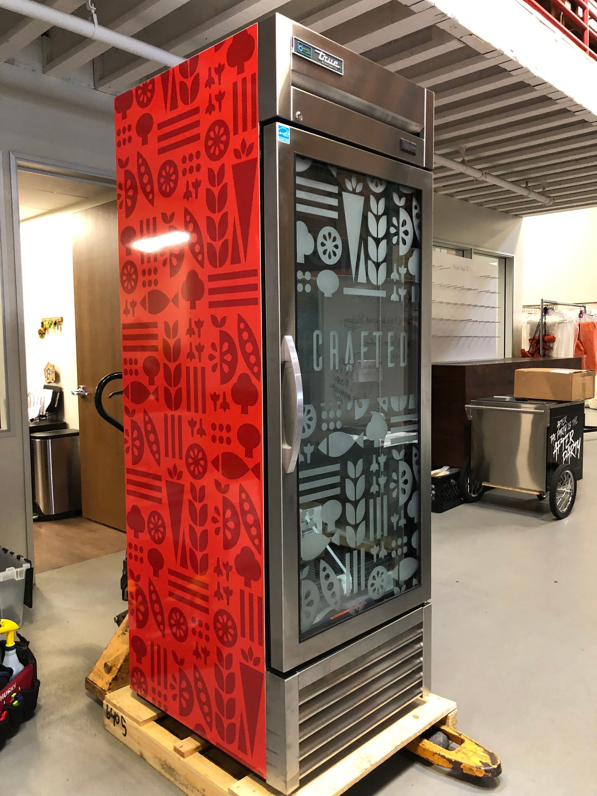 A red refrigerator with a glass door is on a pallet