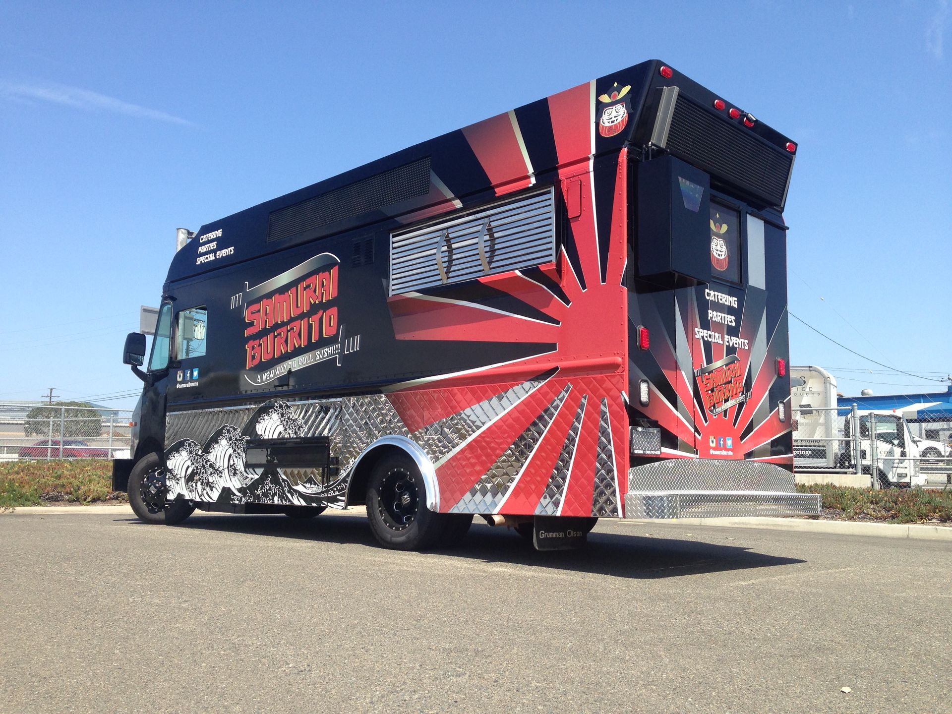 A black and red food truck is parked on the side of the road.