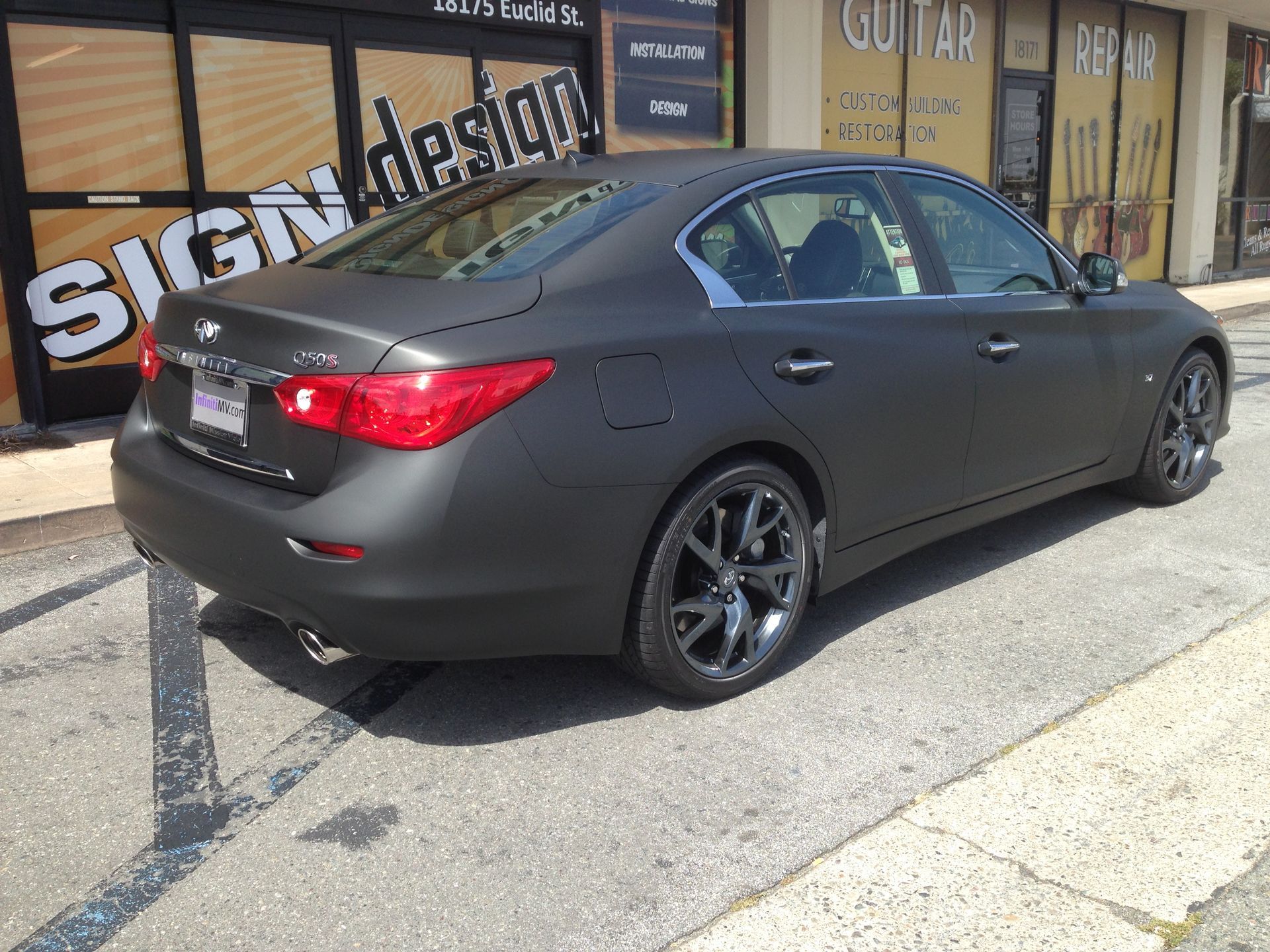 A black car is parked in front of a sign design store