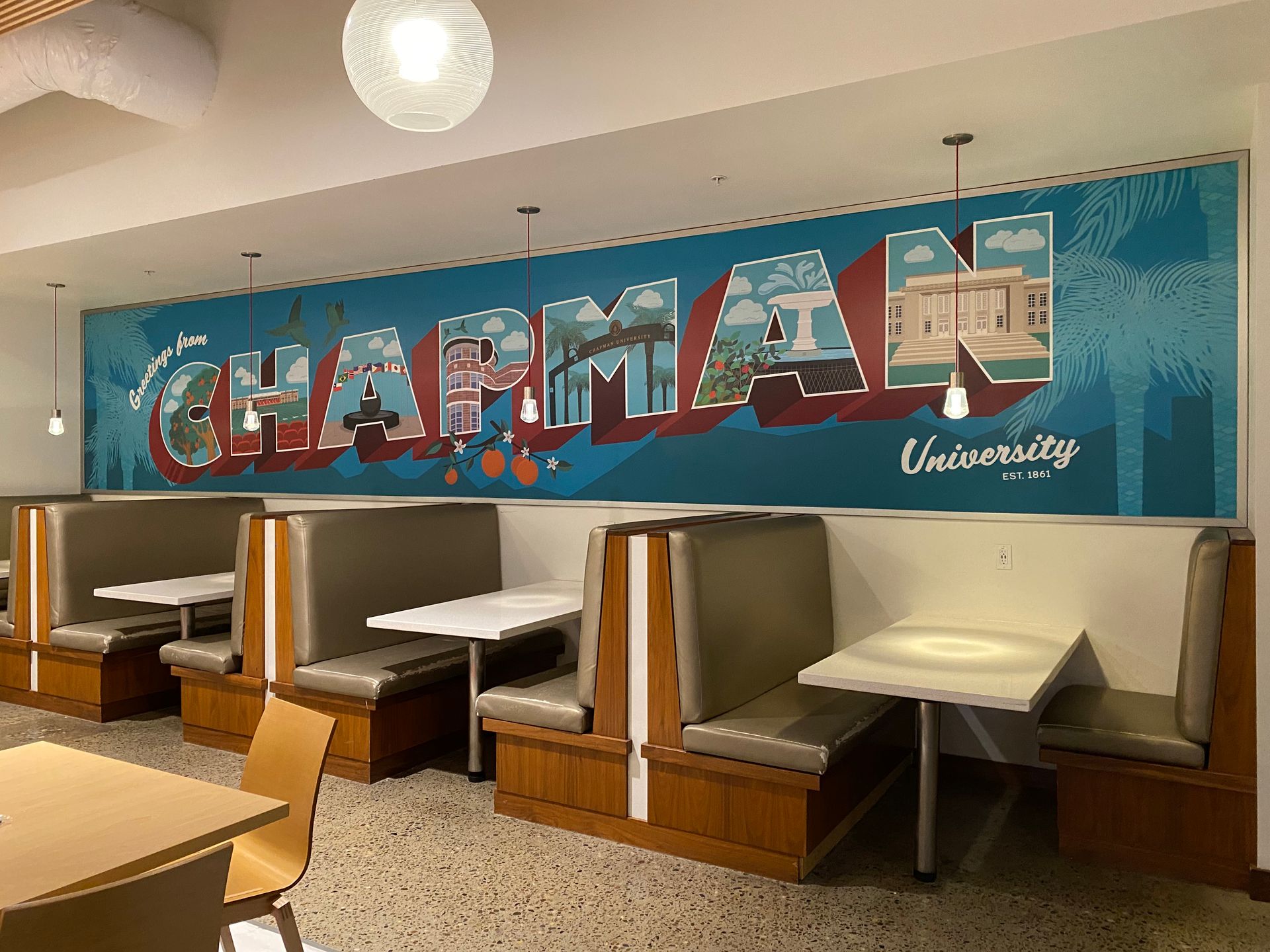 A dining room with booths and tables and a mural that says chapman university