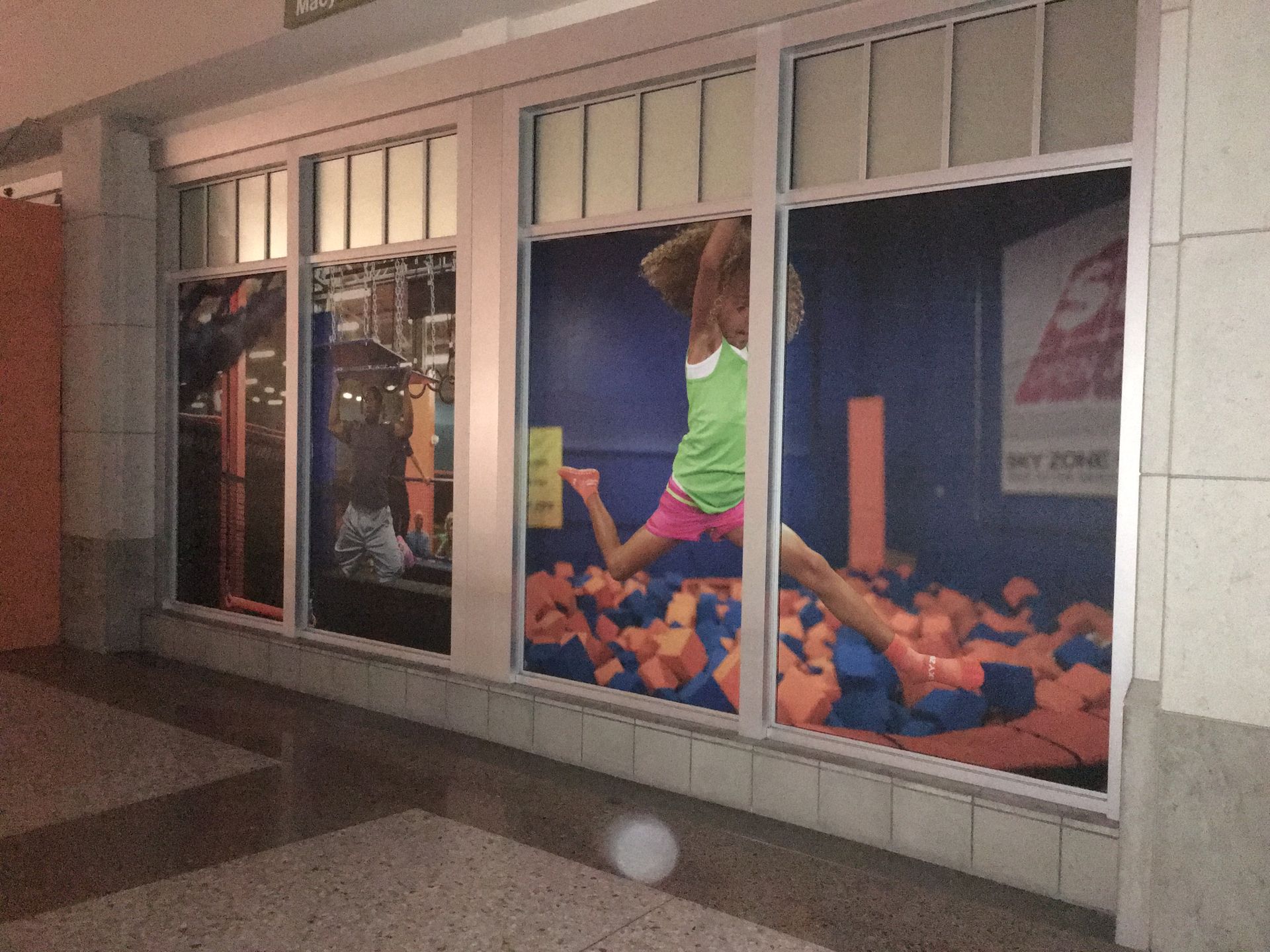 A woman in a green tank top is jumping in a foam pit